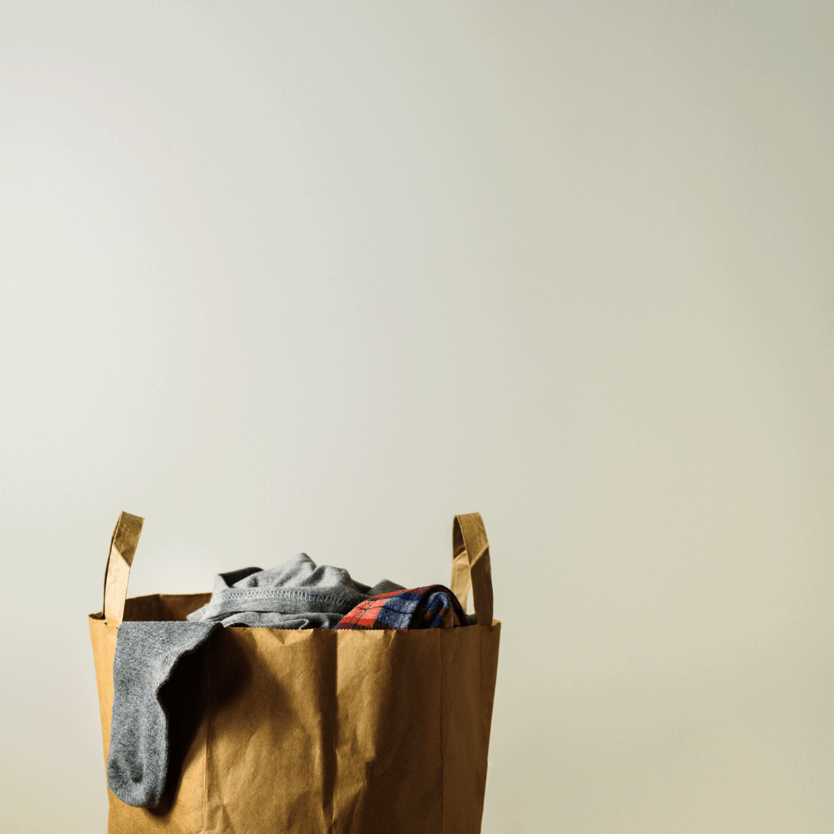 paper grocery sack overflowing with clothes against a white wall
